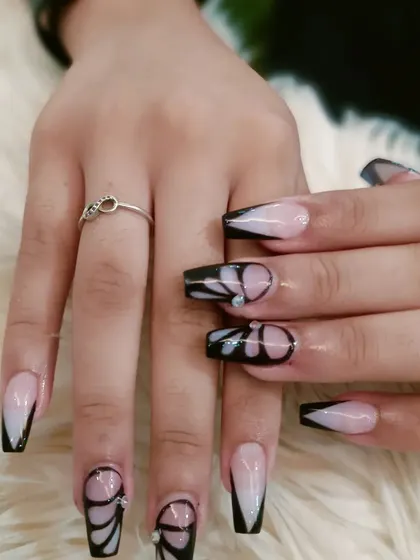 A striking butterfly wing design in black on long, coffin-shaped nails with a soft ombré base.