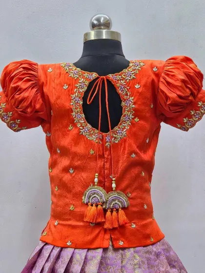 A detailed view of the back of an orange blouse, showing the keyhole design and the intricate embroidery around the neckline.