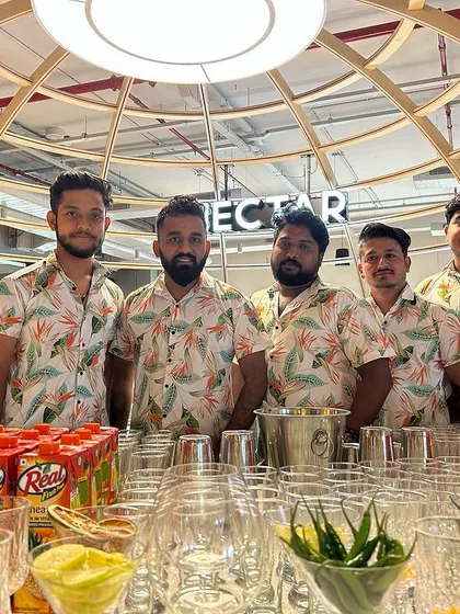 The team posing behind a fully prepped mocktail bar, ready for a corporate event. We handle events of all types, with or without alcohol.