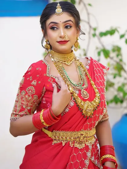 A vibrant bridal look in a red bandhani lehenga-saree. The makeup features a classic red lip and defined eyes, matching the festive and celebratory feel of the outfit.