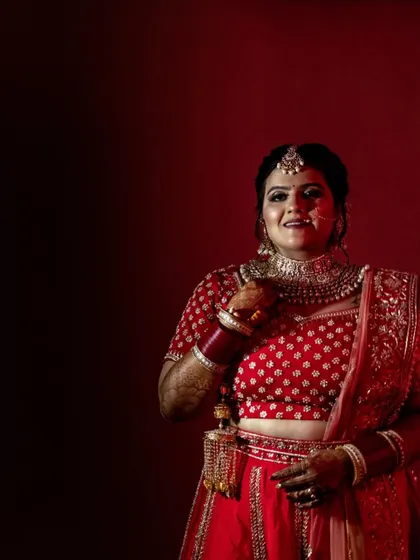 A classic bridal portrait against a rich red backdrop. The bride's smile and traditional attire are the focus, creating a timeless and elegant photograph that she will cherish forever.