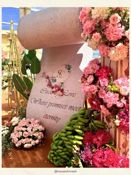 A personalized stone-carved scroll reads "Circle of Love," surrounded by pink florals and traditional elements like bananas, adding a unique and symbolic detail to the wedding ceremony.
