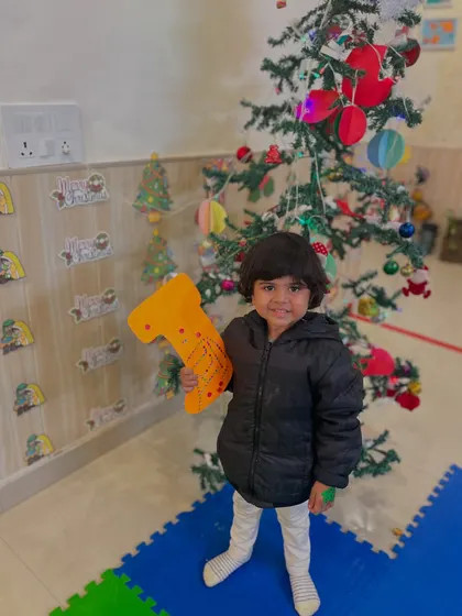 A smiling boy poses with a toy by the Christmas tree, enjoying the festive atmosphere of our workshop.