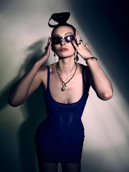 A high-contrast portrait from the Mugler x H&M shoot. The dramatic lighting and pose are styled to accentuate the corset details of the dress and the bold, futuristic accessories.