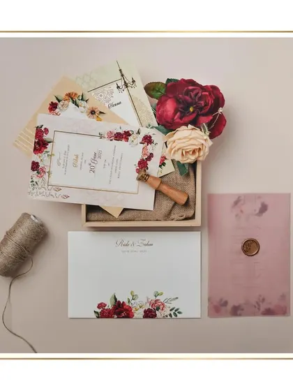 A rustic yet elegant boxed invitation set. The cards feature a beautiful floral design in deep reds and are presented on a bed of jute fabric inside a wooden box, sealed with a custom wax stamp.