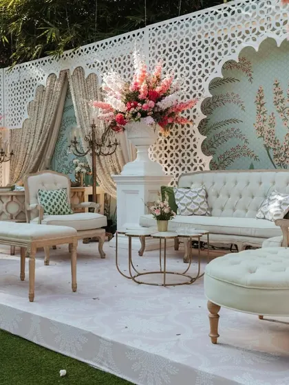 A luxurious seating area with a pastel blue peacock-themed wallpaper backdrop. The design combines classic furniture with vibrant floral arrangements and elegant candelabras for a touch of royalty.