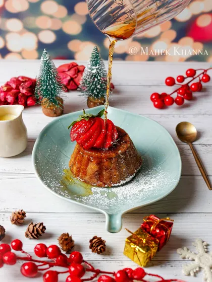 A beautiful Christmas pudding being drizzled with syrup, surrounded by festive decorations.