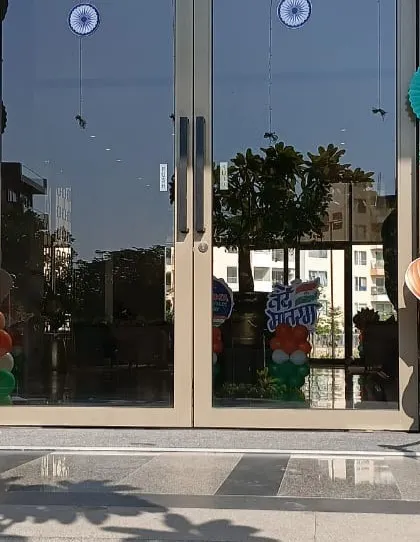 The entrance to this building is decorated with tricolor balloon pillars topped with hot-air-balloon-themed cutouts. The green paper fan decorations add another layer of texture to the Republic Day setup.