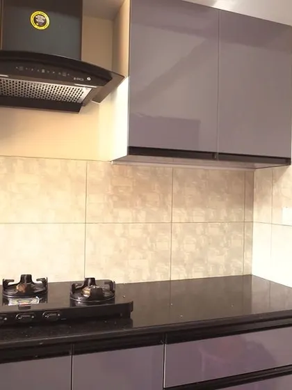 A close-up of the hob and chimney area, set against a simple tiled backsplash. The glossy grey finish of the cabinets provides a modern and easy-to-clean surface.