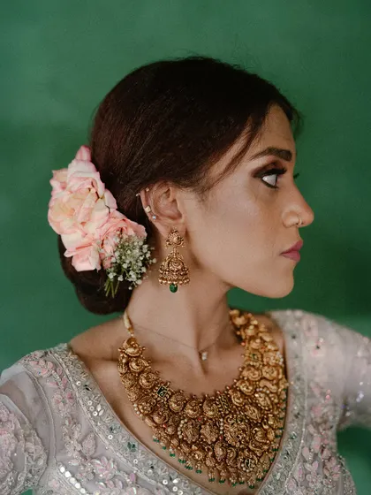 A close-up profile of a bride, showcasing her intricate temple jewelry and the delicate flowers in her hair. This shot highlights the beautiful details of her bridal styling.