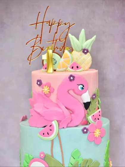 Another angle of the two-tiered flamingo cake, showing the full composition of the flamingo, tropical fruits, and flowers.