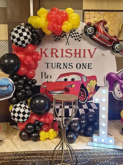 A high-energy Cars theme for Krishiv's first birthday. The setup includes a custom backdrop, character standees of Lightning McQueen, and a balloon arch in the theme's signature red, black, and yellow colors.