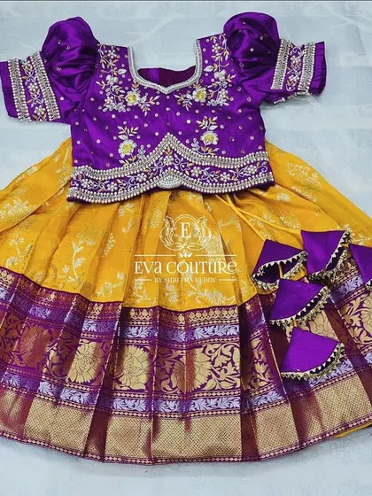 A beautiful yellow and purple pattu lehenga for a toddler. The purple blouse has delicate floral embroidery, and the skirt has a traditional Kanchi-style border.