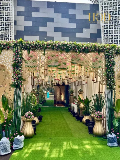 The exterior view of the grand entrance, showing the intricate latticework and floral border. The green carpet running through the center creates an inviting path into the celebration.