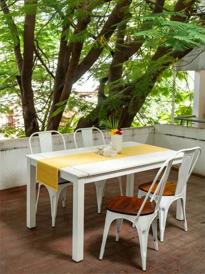 An outdoor dining setup that invites nature to the table. The sleek, white metal table is paired with industrial-style chairs featuring solid wood seats, creating a durable and stylish space for alfresco meals.