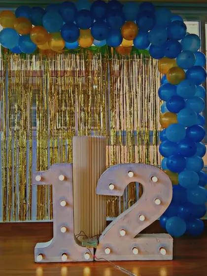 A simple yet impactful setup for a 12th birthday. This decoration features our large marquee number "12", a blue and yellow balloon arch, and a gold shimmer curtain backdrop, perfect for a fun pre-teen party.