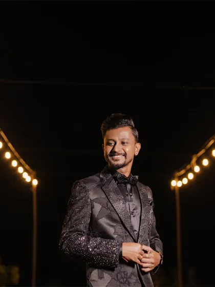 A dapper portrait of the groom in his sparkling tuxedo, smiling under the warm glow of string lights.