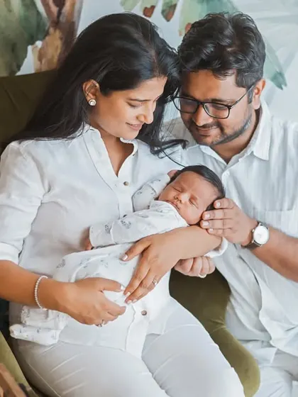 A beautiful family portrait with their newborn. The all-white outfits and the natural, leafy background create a fresh, clean, and serene atmosphere.