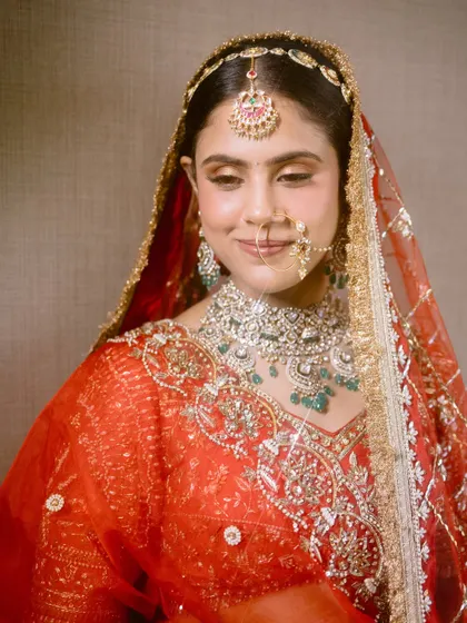 This bride's regal red outfit is paired with a classic makeup look, featuring defined eyes and glowing skin, perfect for her wedding ceremony.