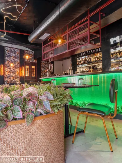 A large woven planter filled with lush greenery sits beside the glowing green bar at Burosu. We used natural elements to soften the industrial and neon features, creating a balanced and texturally rich environment.