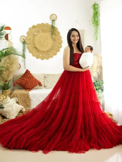 A stunning portrait of a mother in a flowing red gown, holding her newborn baby. The contrast of the red dress against the neutral background is striking.