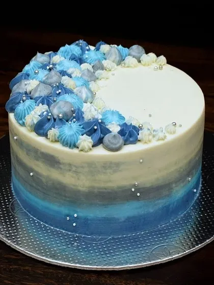 This popular design features a blue and grey watercolor effect on the sides. The top is adorned with a crescent of piped buttercream swirls in coordinating shades of blue, grey, and white.