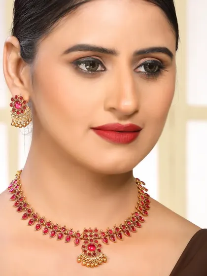 A model wearing a traditional gold necklace set with vibrant pink stones, showcasing ethnic jewellery for festive occasions.