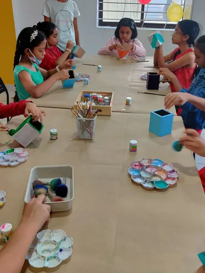 A wide shot of the party table where kids are busy painting pen stands and other fun items.