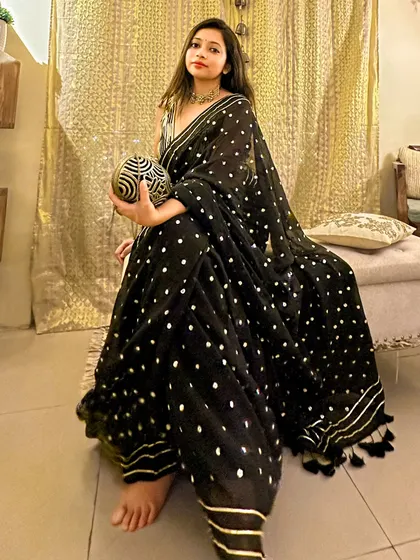 A full-length shot showing the beautiful fall of the black mul cotton saree. The fabric is light and comfortable, but the sequin and gota patti work make it festive enough for a wedding.
