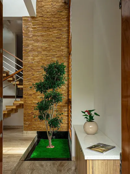 The entrance to the Cube House greets you with an internal courtyard under a skylight. This design immediately establishes the home's connection to nature and light, with a stone accent wall and a small tree.