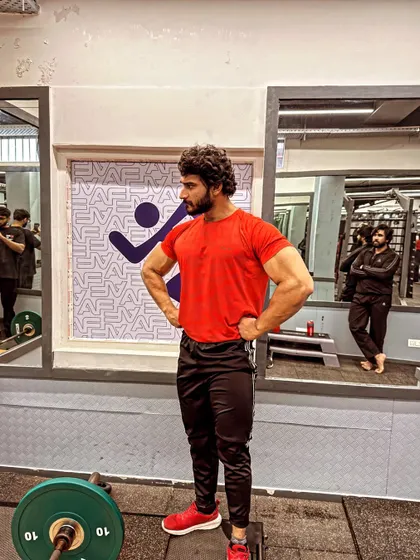 Day 81 of 100. Standing by the weight plates, feeling the energy of the gym. The goal is clear: Mr. Delhi.