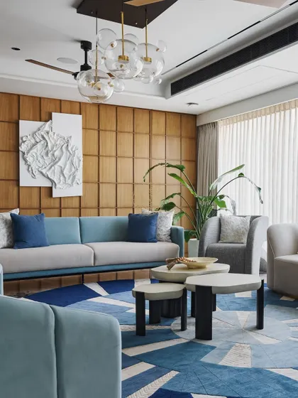 Another seating area in the same duplex, with a pastel blue sofa set against a wood-paneled wall. The abstract white wall art adds texture, and the space is designed to feel open and airy.