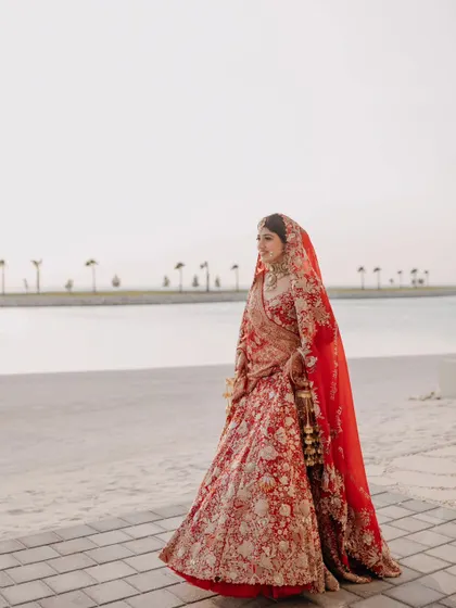 A breathtaking portrait of the bride in her magnificent red lehenga, standing by the water. This shot captures her elegance and the beauty of the seaside location.