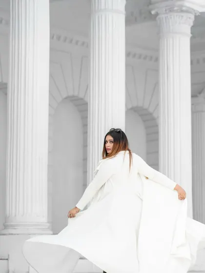 A dramatic, high-fashion shot with the model in a flowing white coat against white architectural columns. The monochrome palette creates a powerful and artistic image.