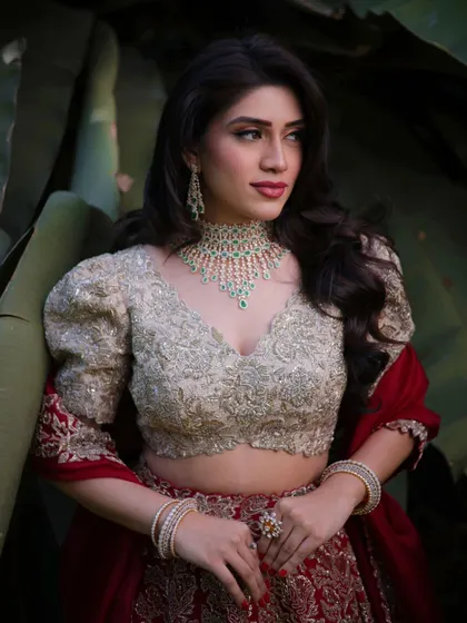 A close up portrait of Mahima. The makeup enhances her features beautifully, with a focus on flawless skin and softly defined eyes, paired with an elegant emerald necklace.