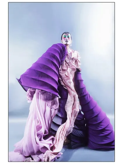 A wide shot capturing the full, expansive form of the avant-garde purple and pink gown. The model stands as a living sculpture, representing the magnificent result of a transformative reaction.