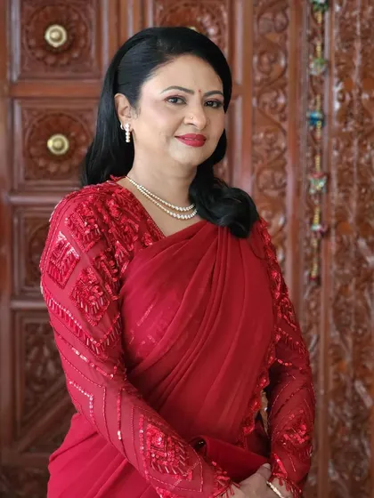 A portrait of a lady in red. The makeup is sophisticated and polished, designed to complement her designer saree and diamond jewellery.