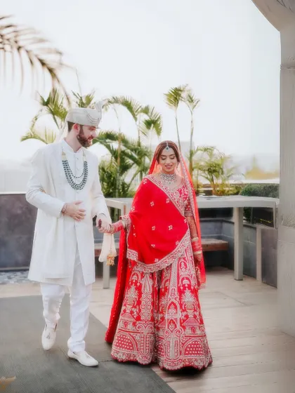 A candid shot of the couple walking hand-in-hand. This natural, in-motion photo captures their connection and the beautiful flow of the bride's red lehenga.