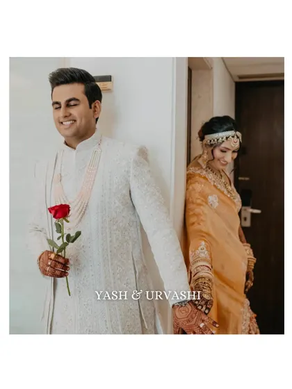 A playful and romantic "first look" style photo, where the couple is separated by a wall. The groom holds a rose, adding a touch of classic romance to this candid wedding moment.