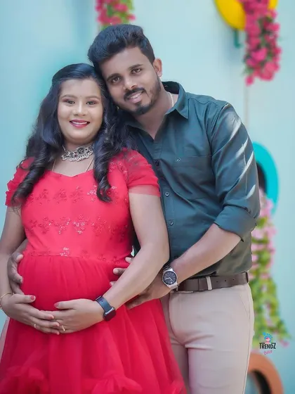 This couple chose a vibrant red gown for their indoor shoot. The colorful backdrop with hanging flowers adds a playful and happy touch to their portrait.