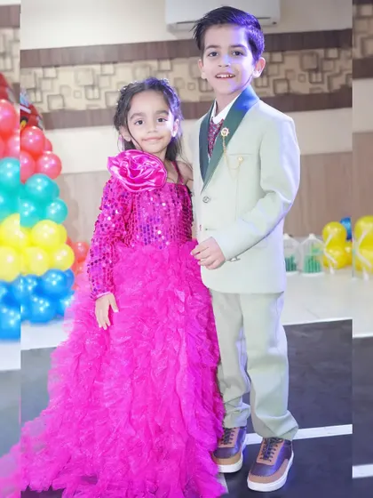 A brother and sister dressed in their party best, posing for a photo during a birthday event.