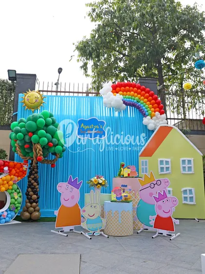 The main stage of the Peppa Pig party, featuring a large backdrop, a balloon rainbow, and character standees for the ultimate photo op.