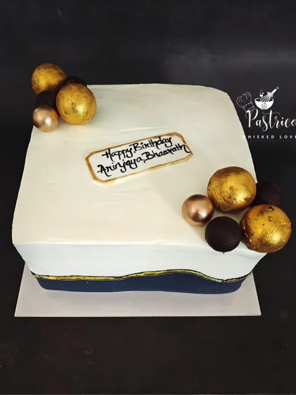 A modern and minimalist square cake with clean lines, a navy blue accent, and elegant gold and chocolate spheres.