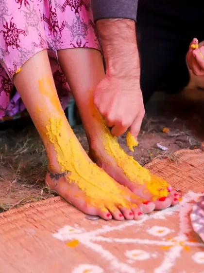 A close-up of the Haldi ritual, showing turmeric paste being applied to the bride's feet. It’s a detail shot that tells a story about tradition and family participation.