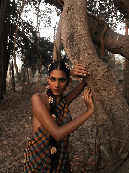 An engaging portrait from the "தெய்வீகம்" (Divinity) series, where the model's direct gaze connects with the viewer amidst a rustic, natural setting.