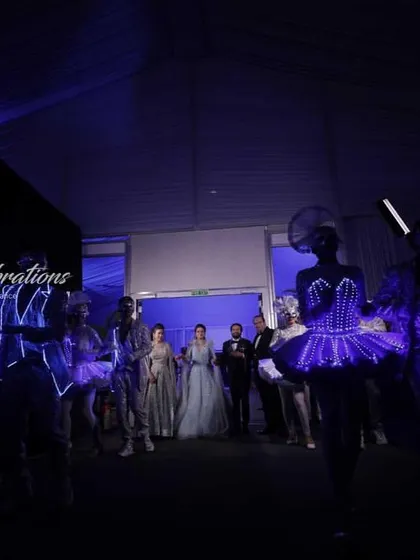 A wide shot of a sangeet entry, showing the couple about to enter a room filled with performers in glowing LED costumes. The anticipation and moody lighting create a dramatic effect.