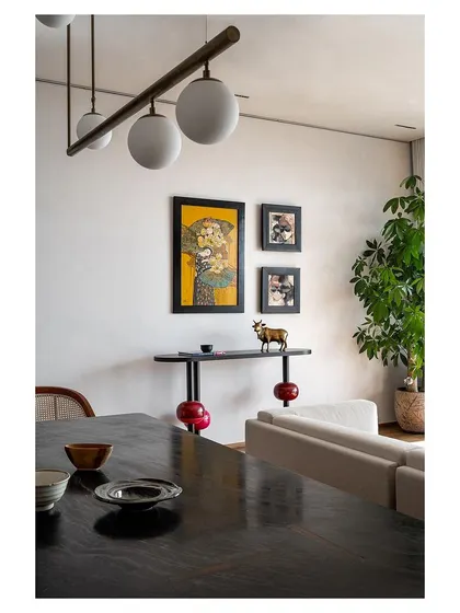 A detail shot showing the layering of art and custom furniture, including a console table with lacquered legs, against the backdrop of the dining area.