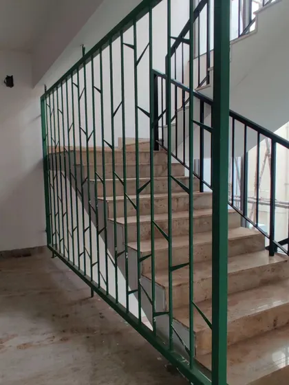 A custom green metal railing for the apartment staircase, with a design inspired by the branching patterns of trees.