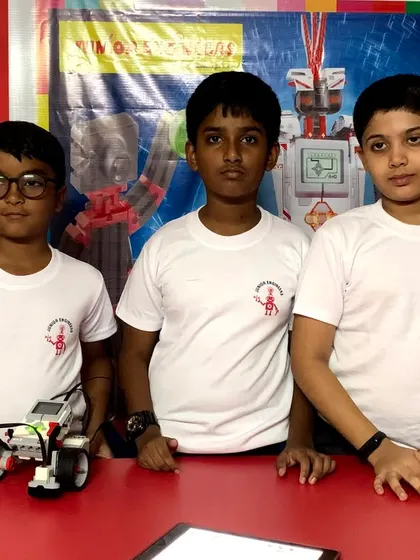 A team of three young engineers presents their competition-ready robot, showcasing their collaborative building and problem-solving skills.