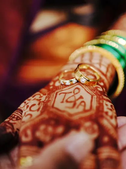 A detailed shot of the engagement rings on the bride's hand, with her mehendi featuring their initials.